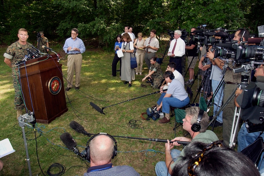 Dave Lapan, wearing a military uniform, speaks to reporters from a podium outdoors.