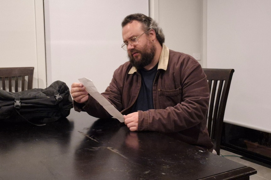 A man sitting on a table looking at a receipt.
