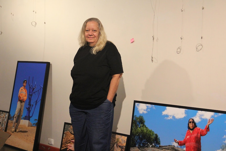 A woman with her hand in pockets, print photos in frames leaning against a wall yet to be hung up.