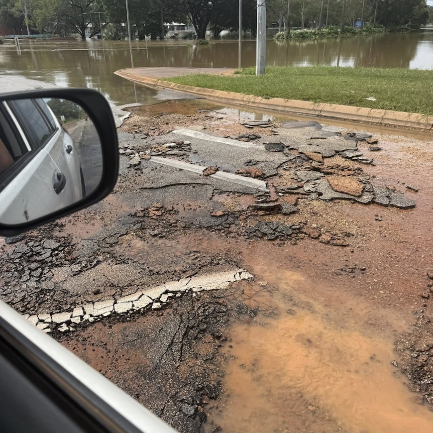 Parts of a road have been ripped up, floodwaters are visible nearby.
