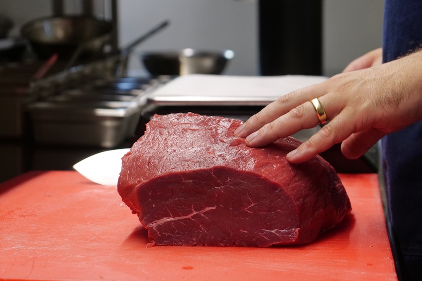 Man cuts into large slab of meat.