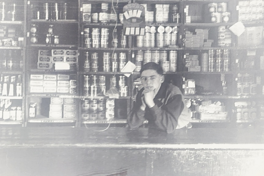 A black and white photo of a man behind the counter of a regional general store.
