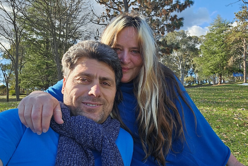 A woman puts her arm around a man's shoulder as they look at the camera smiling.  
