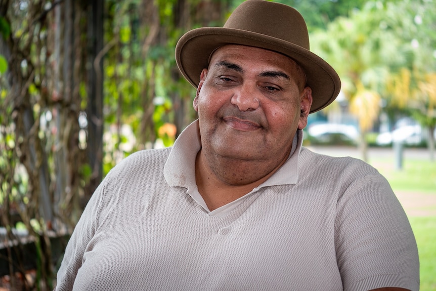 Man in a grey shirt and hat smiling.