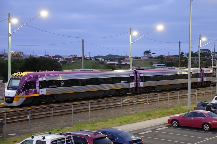 An overcast day. A purple and yellow regional train exits the platform at Warrnambool in the early morning.
