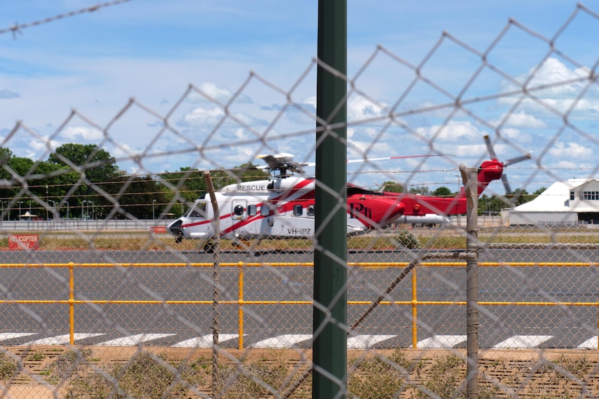 a rescue helicopter viewed through a cyclone fence at an airport.