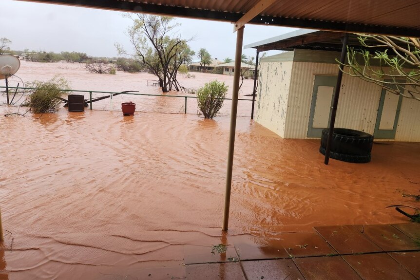 Floodwater surrounds a shed and laps at paving beneath an awning on an outback station.