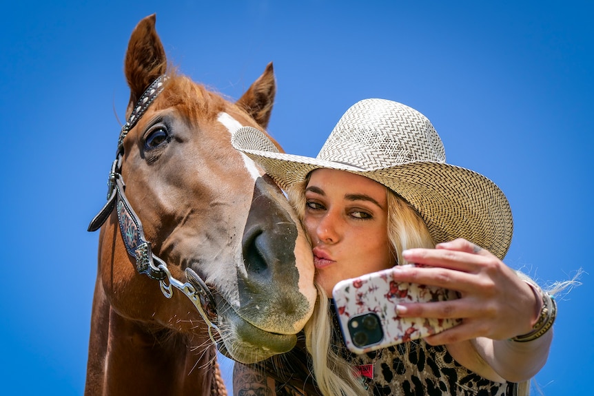 Storm Hogan kisses her horse Barbie on the nose while taking a photo with her mobile phone