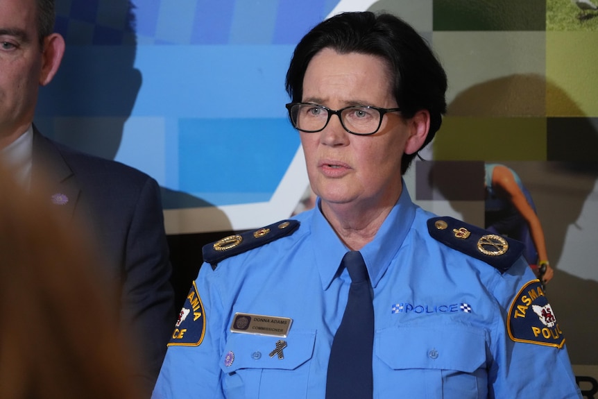 A woman with dark hair and glasses in a police uniform talks at a media presser