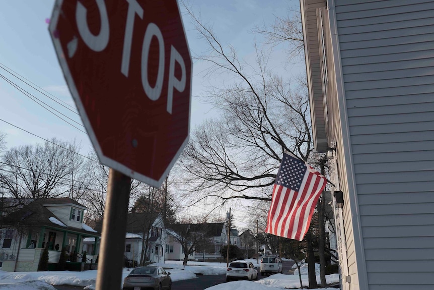 A stop sign is seen in the foreground while an American flag flies from a white house in the background. 