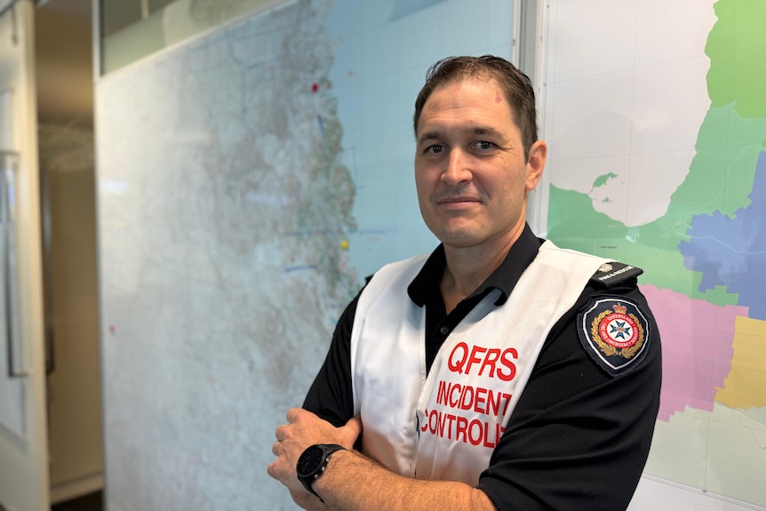 A man standing in front of maps with his arms crossed, QFD uniform on