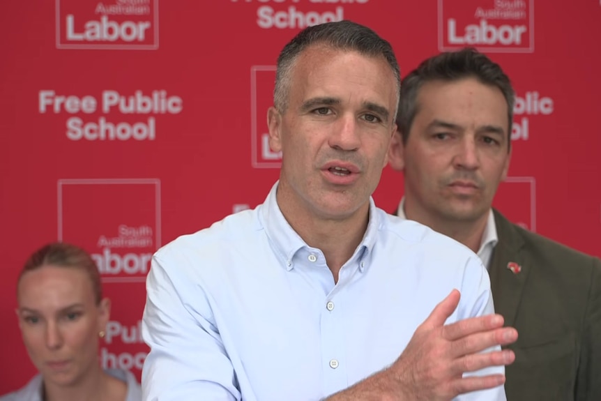 A man in a white shirt talking at a press conference