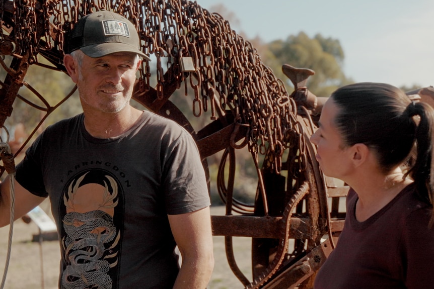Sam Anderson smiles while touching his giant sculpture of a horse using recycled materials, and talks to Myf.