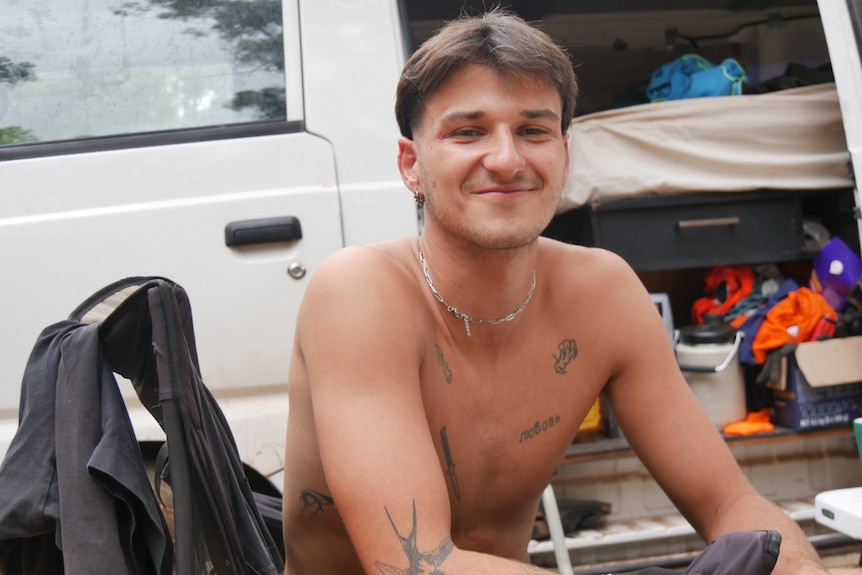 A shirtless man with tattoos smiling.