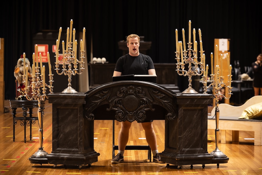 A blonde man standing behind a piano with candelabras