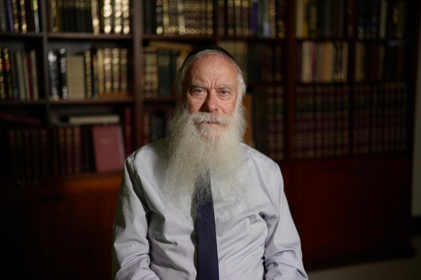 A man with a long beard standing in a dark room.