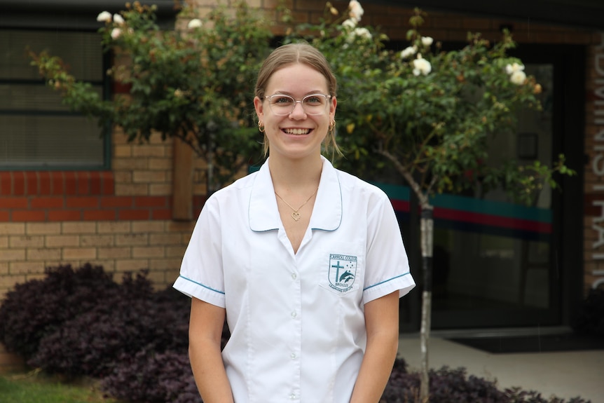 A female student in her school uniform and glasses smiles at the camera.
