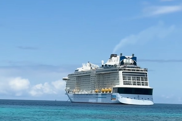 A large cruise ship sits in shallow water under a blue sky