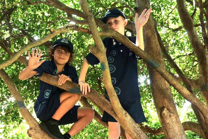 Two boys wearing dark blue school uniforms, climbing a tree.