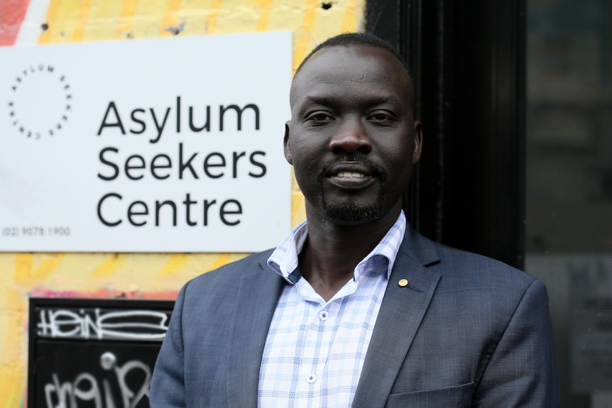 Elijah has dark-coloured skim and wears a suit jacket, posing for a photo.