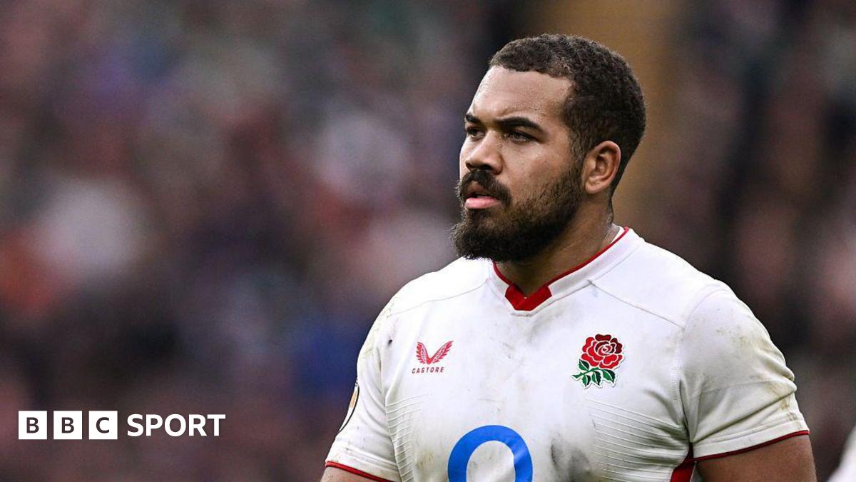 Close-up of England's Ollie Lawrence. He has short black hair and a beard, and is wearing a white shirt which has the English team's crest - a rose - on the left breast and manafacturer's logo on the right.