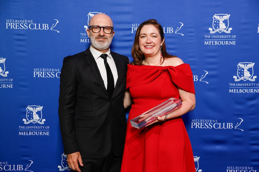 A man and a woman smile while receiving an award at a ceremony in Melbourne. 