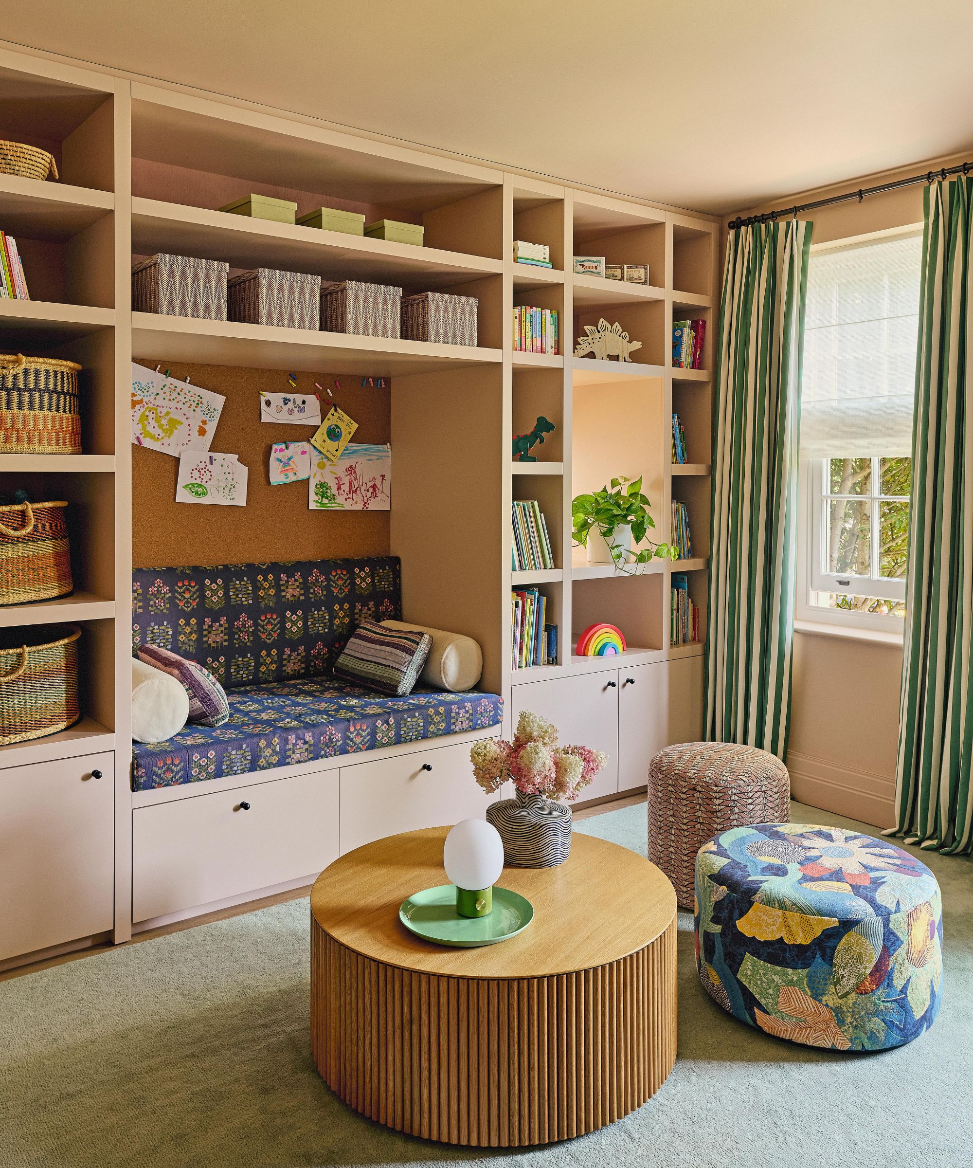 a soft pink playroom with custom cabinetry, built in bench seat, a round oak coffee table and upholstered poufs