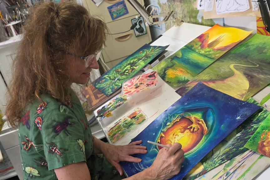Lady drawing at her desk, looking down at her artwork.