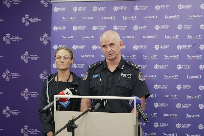 A man in a police uniform, speaking into news microphones.