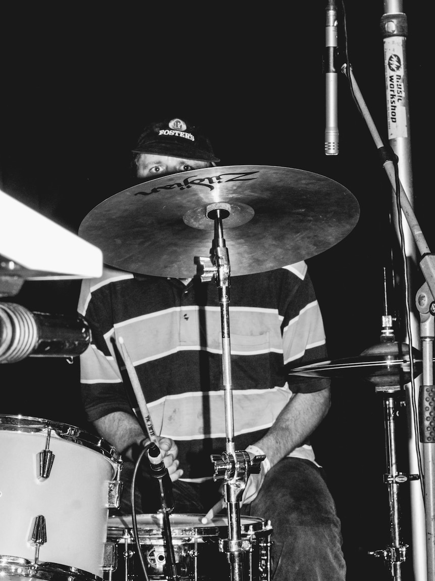 Black and white photo of a drummer with only his eyes visible behind a drum kit