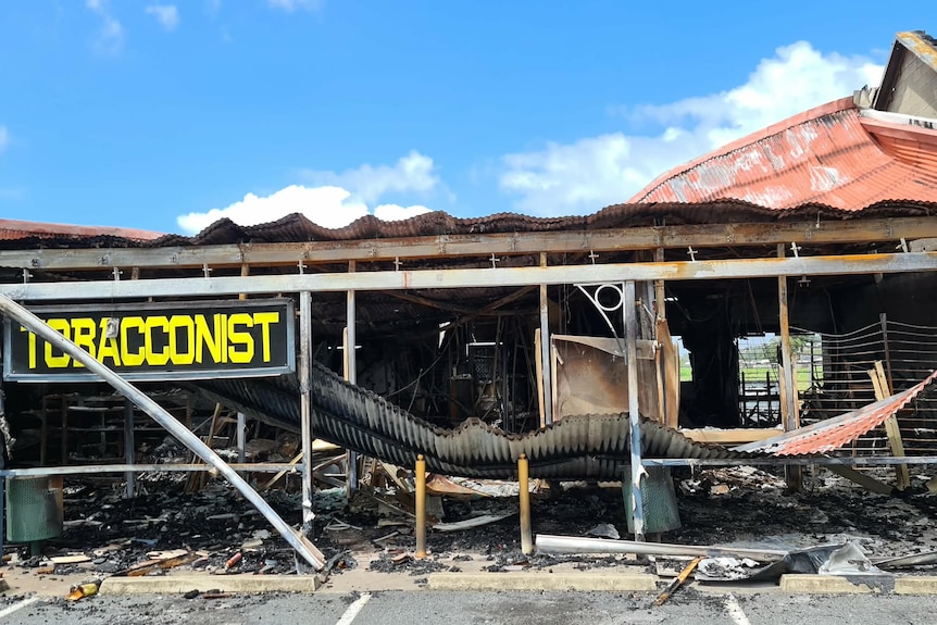 A medium shot of a burnt tobacconist shop, with the sign left as the only thing not burnt. 