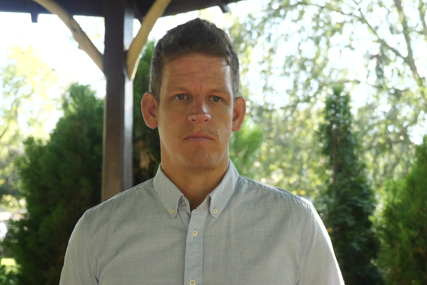 A man with trees behind him looks serious