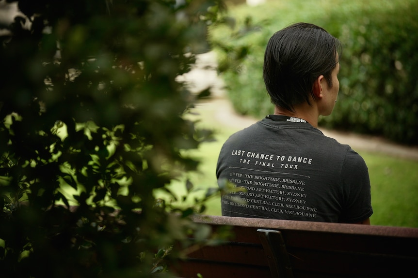 a man sits with his back to the camera on a park bench 