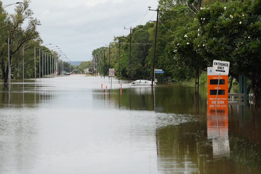 A street flooded by water as far as the eye can see, with a small silver car submerged in the distance. 