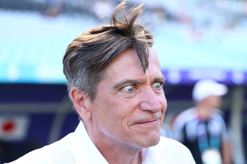 A man in white with grey hair has his eyes wide open