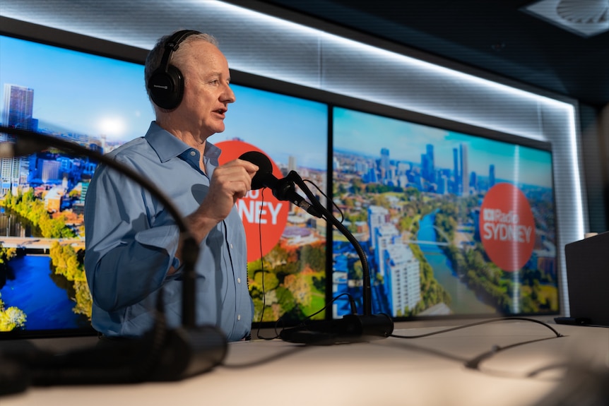 Hugh Marks gesturing while speaking into a microphone in a radio studio.