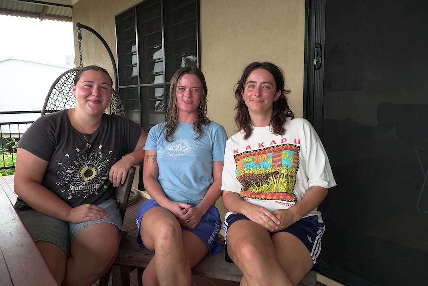 Three young woman sit on a verandah
