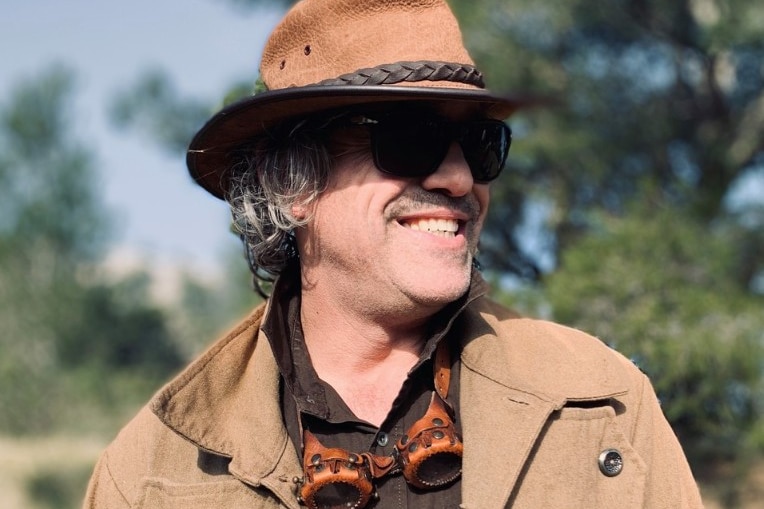 A 54-year-old man, smiling, and wearing a hat.
