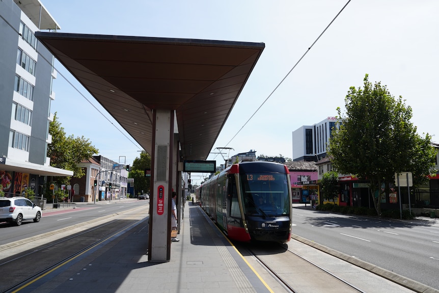 A light rail vehicle pulled up next to a stop with a roof on a cloudy day.