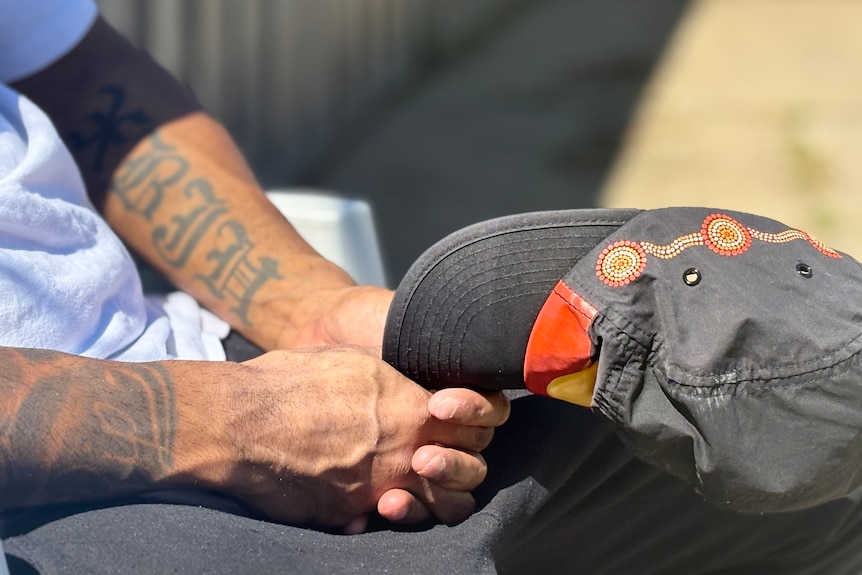 A close up photo of a man's hands holding a hat with the Aboriginal flag on it.