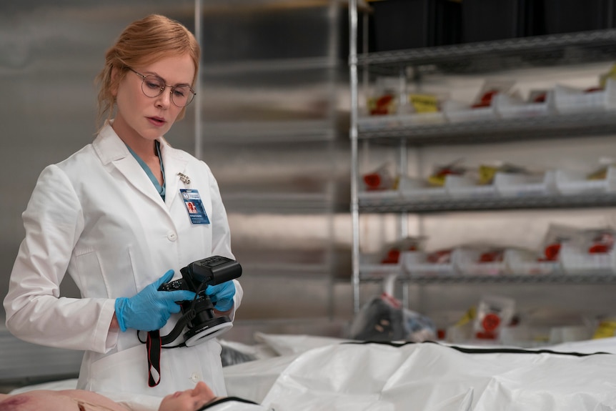 A woman in a white lab coat conducts work in a morgue