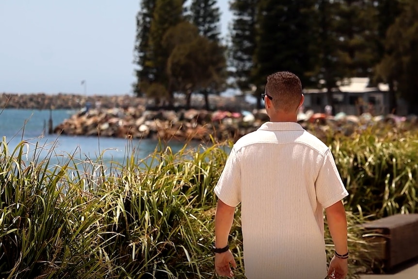 A man in a white t-shirt walks on a pathway beside the ocean.