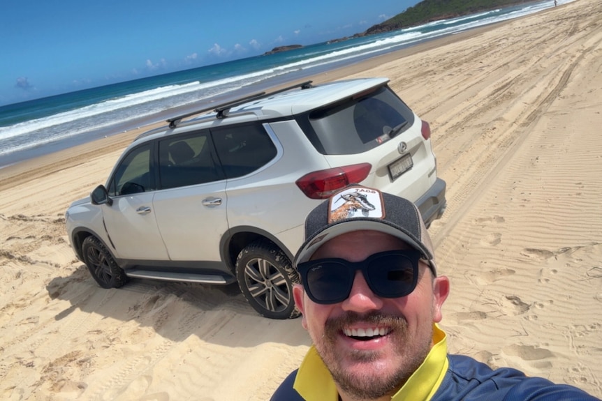 A man stands in front of a four wheel drive on a beach