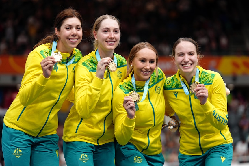 Four women with medals on a podium, smiling