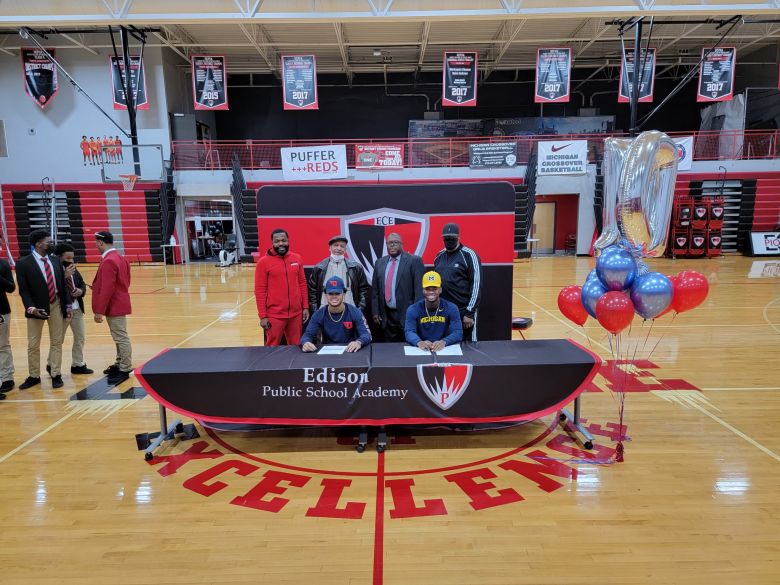 Greg Pace Jr. sits in front of a backdrop on a basketball court.