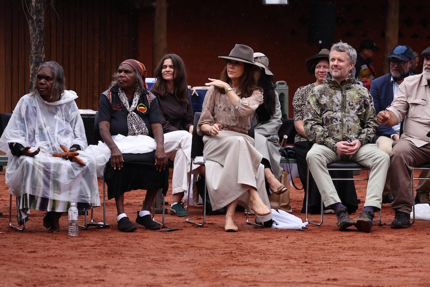 Mary and Frederik sit on chairs watching a man perform a ceremonial dance