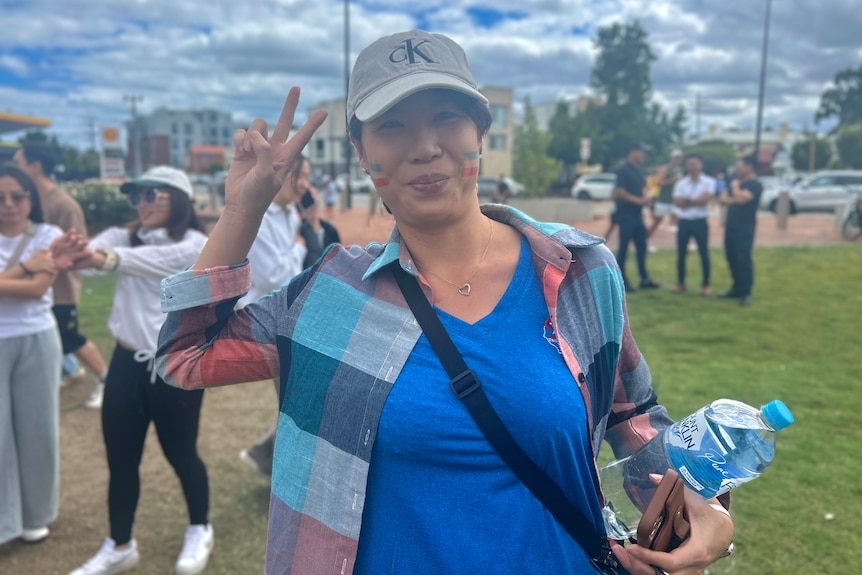 A woman in a blue shirt smiles and makes the peace sign with her hand