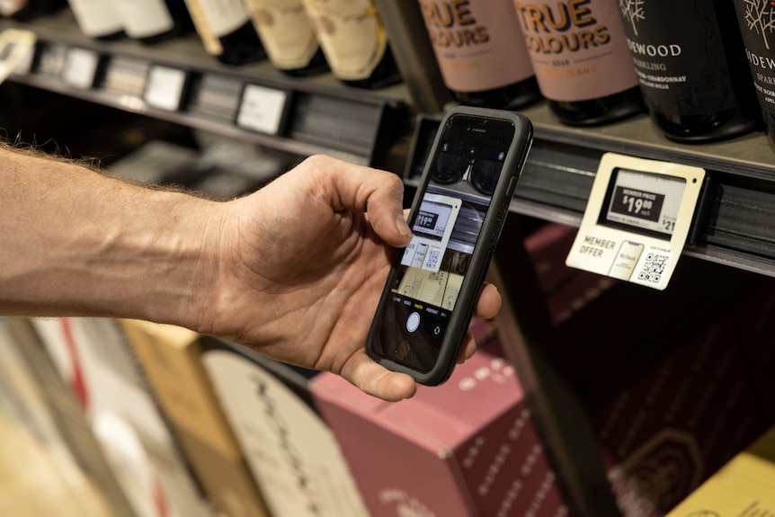 A man's hand holding an iphone scanning a label at Dan Murphy's liquor shop.