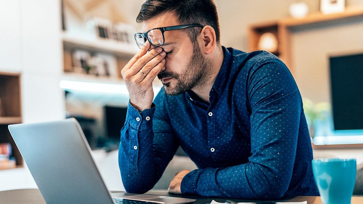 Tired young businessman working at home using lap top and looking Anxious