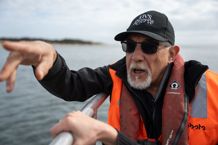 Man in high vis jacket on boat pointing off screen